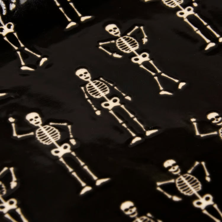 A close-up of a glossy black tray covered with  cream-colored skeleton figures in different poses.