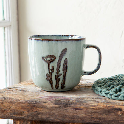 white ceramic mug with brown botanical design set on rustic wooden surface