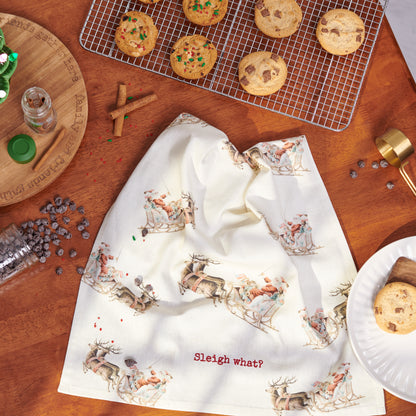 "sleigh what" towel draped on a kitchen counter with a cooling rack of cookies and spices arranged around it.