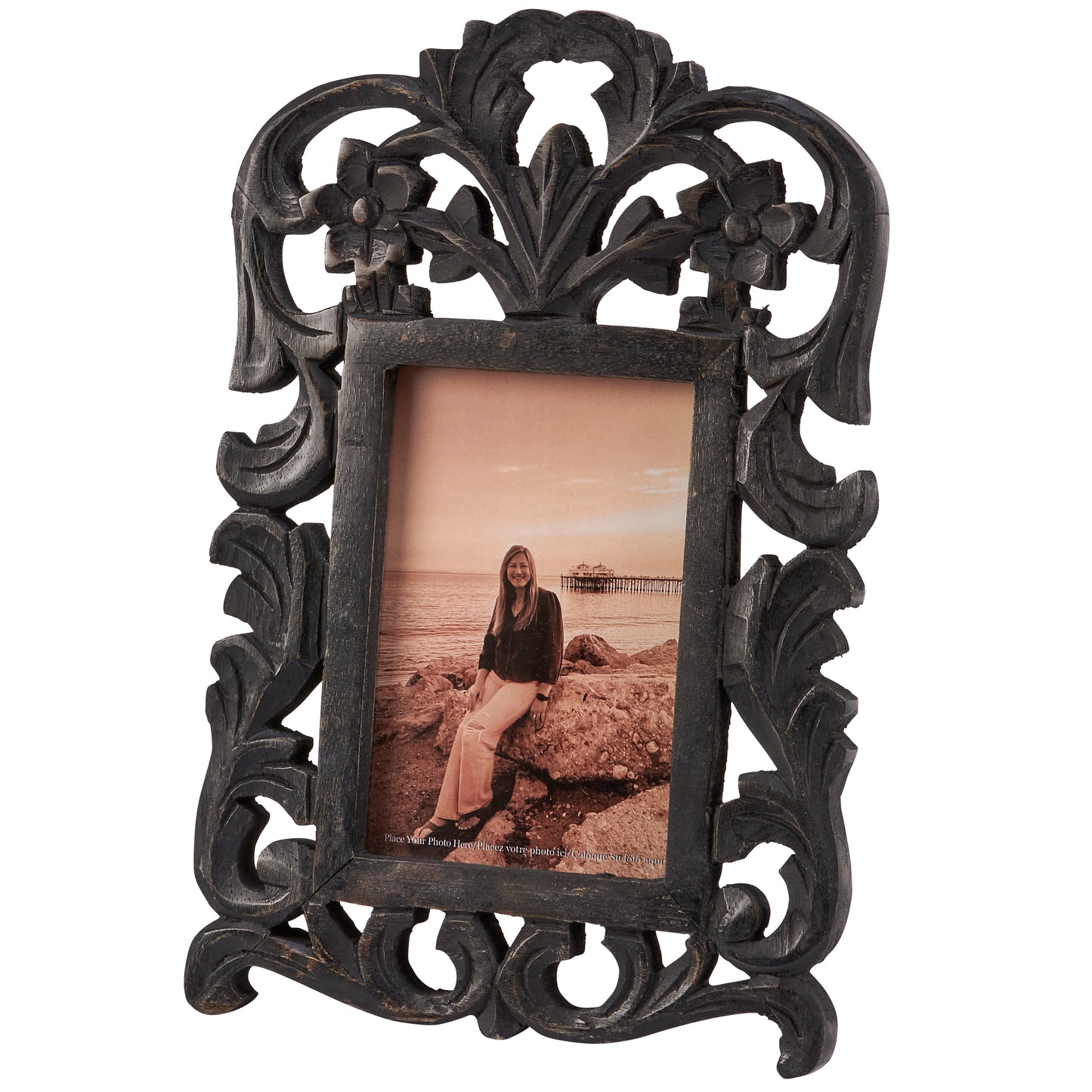 A black filigree photo frame with a photo of a woman sitting by the beach in it