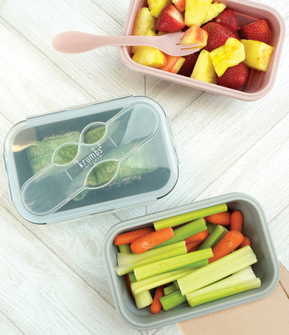 top view of silicone containers, one filled with veggies, one with fruit, and on with a wrap.