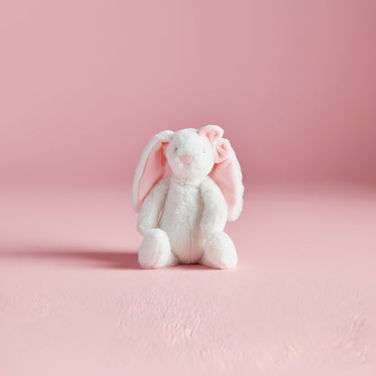 White plush bunny with pink interior ears and pink bow on one ear toy on a pink background