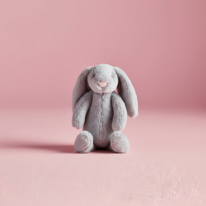 light grey plush bunny seated on a pink background