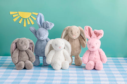 Five plush bunny toys in different colors on a blue checkered tablecloth with a light green background with paper sunshine.