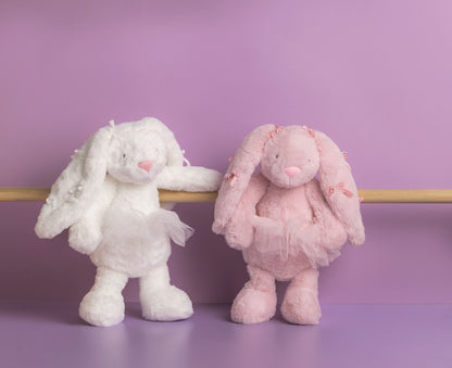 Two plush bunny toys, one white and one pink, on a purple surface with a purple background.