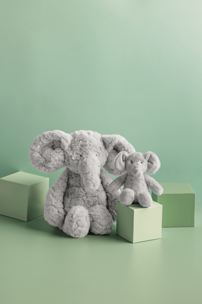 Two gray plush elephants on green blocks against a light green background
