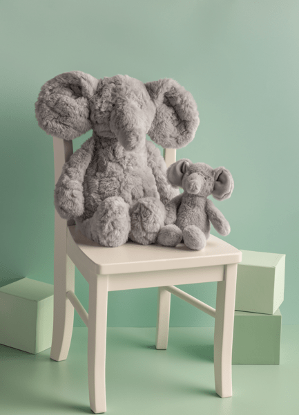 Two gray plush elephants on a small white chair against a light green background