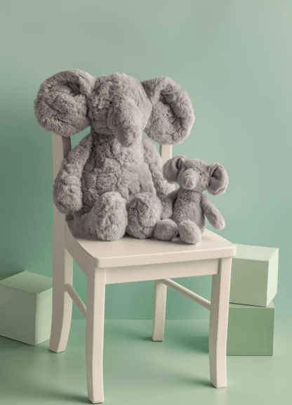 Two gray plush elephants on a small white chair against a light green background