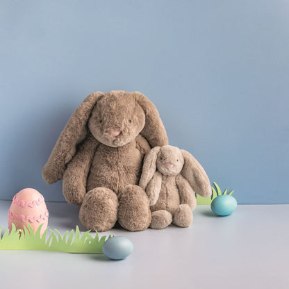 Two brown plush bunnies with Easter eggs and grass on a light blue background
