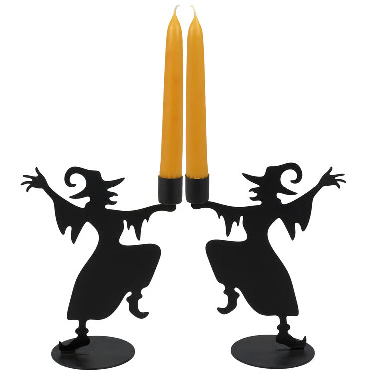 2 black witch-shaped candle holders with two tall orange taper candles inserted, shown against a plain white background.