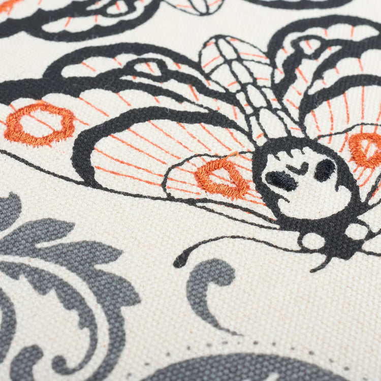 Close-up of embroidered moth design on fabric with black, orange, and gray colors.
