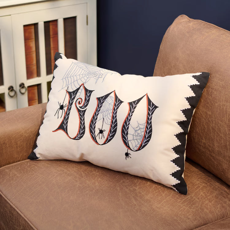 Decorative pillow with Halloween-themed design on a brown couch.