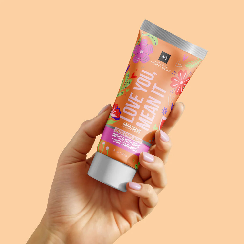 Hand holding a tube of 'Love You Mean It' hand cream against an orange background