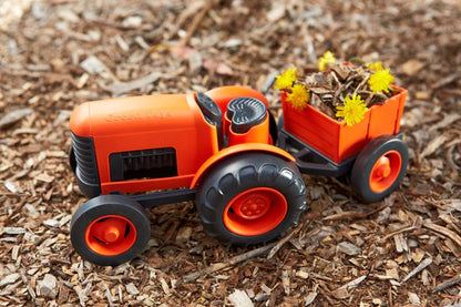 orange tractor with trailer set in the dirt, trailer is filled with leaves and flowers.