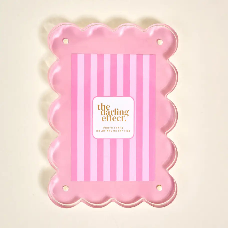 A pink scalloped photo frame with a pink and white striped insert card in the center, featuring a white label that reads 'the darling effect' 
