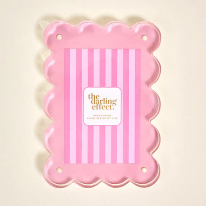 A pink scalloped photo frame with a pink and white striped insert card in the center, featuring a white label that reads 'the darling effect' 