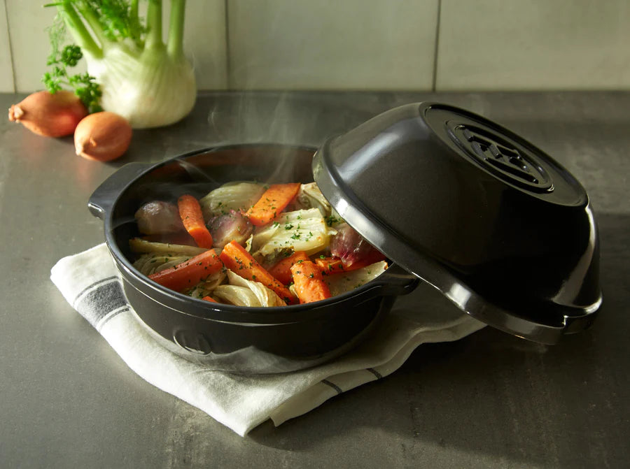 pot set on a towel on a countertop with steaming veggies in it and lid set askew on it.