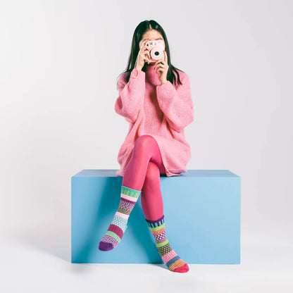 person wearing pink sweater and legging and Dahlia Crew Socks sitting on a blue box holding camera to their face