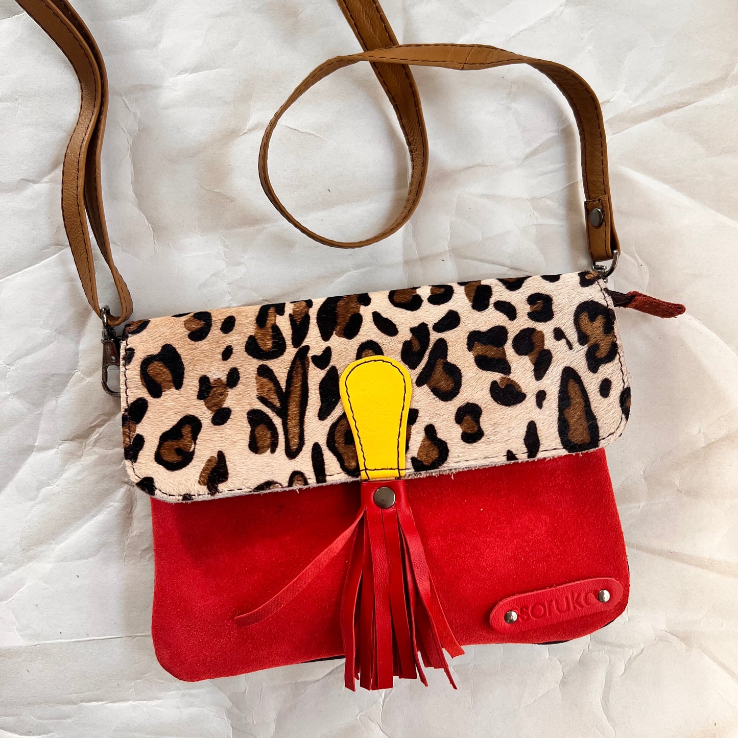 juliette bag with animal print flap, red tassel, and crossbody strap clipped on it.