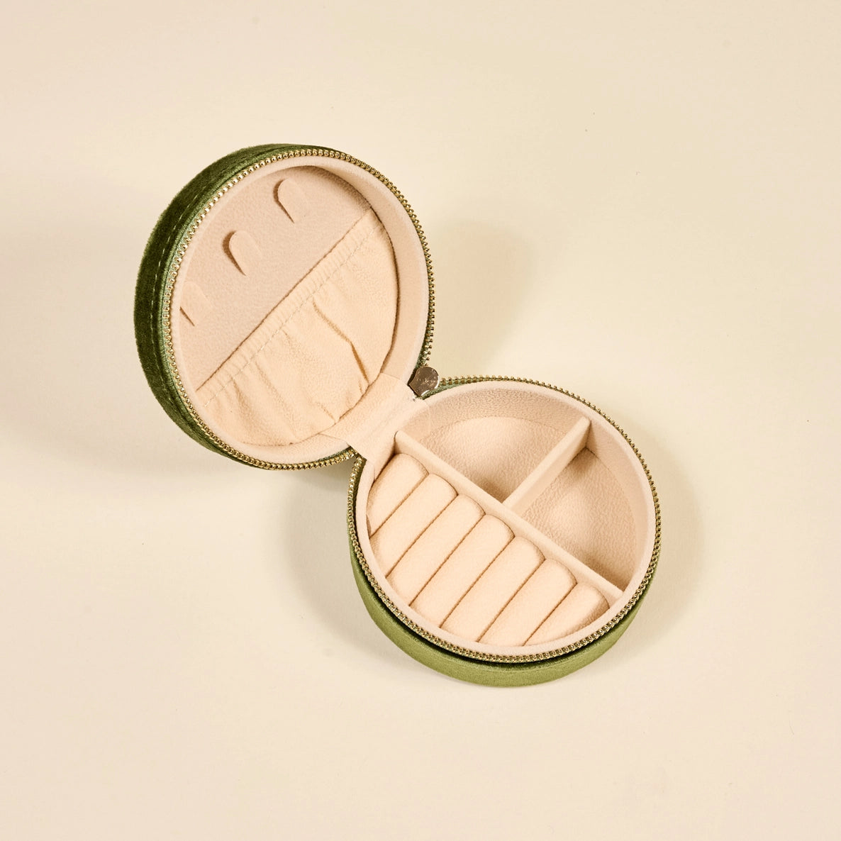 Round jewelry case with green exterior and beige interior with slots and compartments for jewelry shown on a beige background