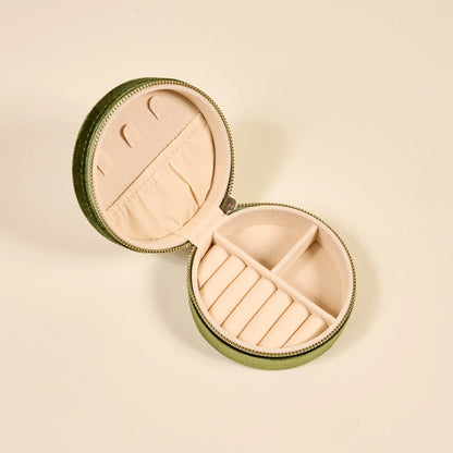 Round jewelry case with green exterior and beige interior with slots and compartments for jewelry shown on a beige background