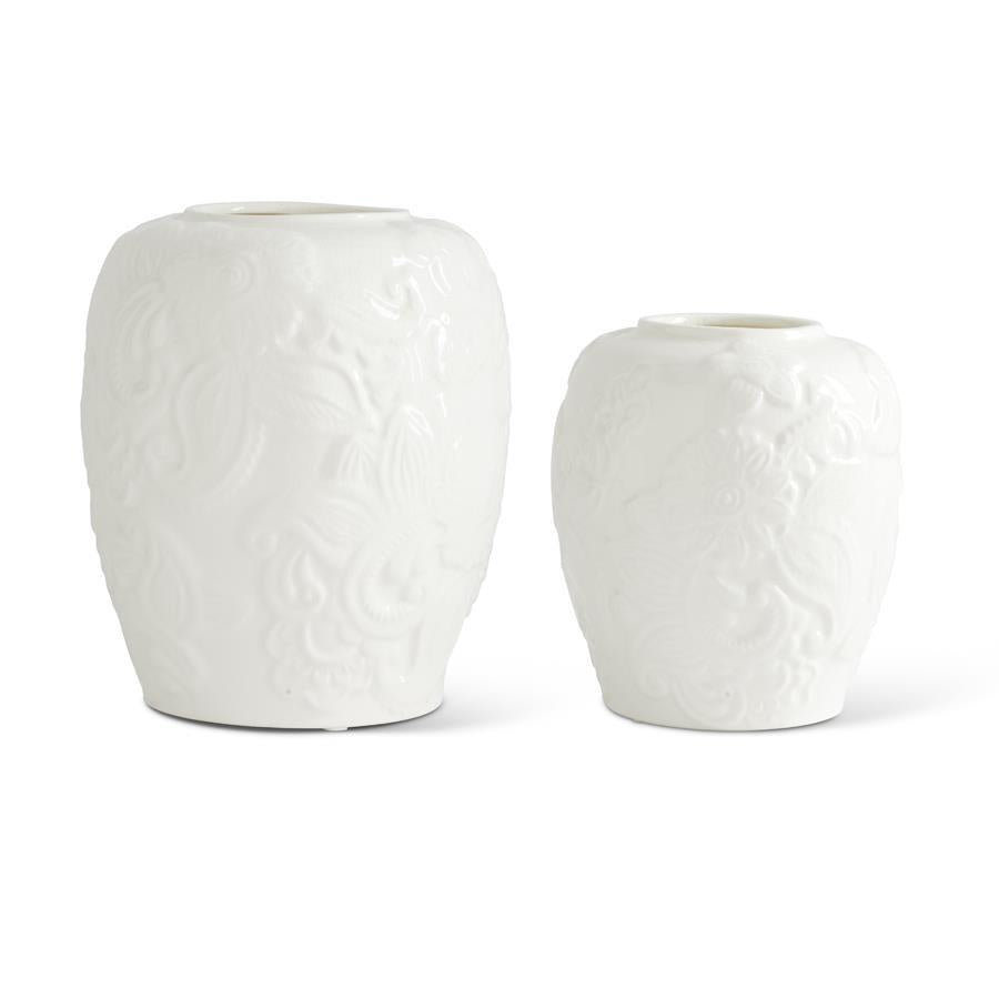 2 white ceramic vases of different sizes with embossed floral designs on them