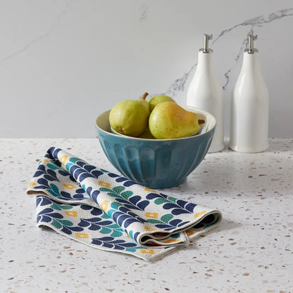 Colorful leaves dish towel draped with its floral side showing on a counter top next to a bowl full of pears.