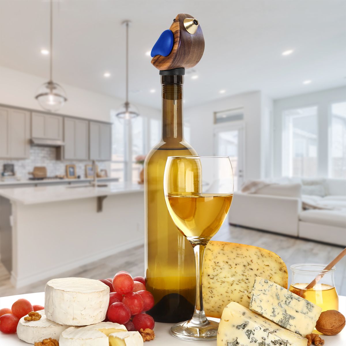 Wine bottle with birdsong bottle pourer in it, glass of white wine, and cheese platter in a modern kitchen.