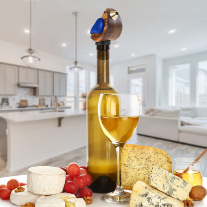 Wine bottle with birdsong bottle pourer in it, glass of white wine, and cheese platter in a modern kitchen.