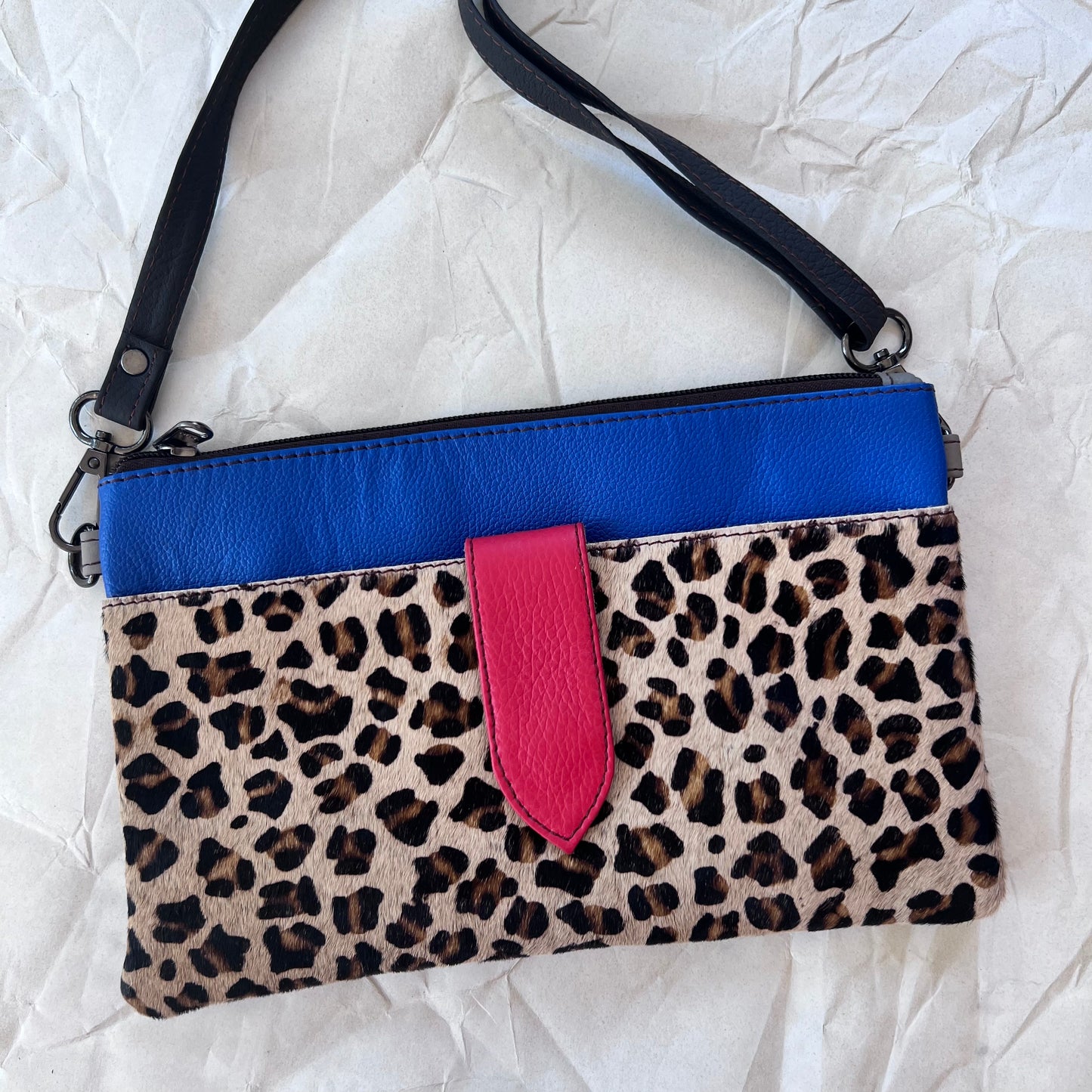 blue rectangular bag with cheetah print pocket, purple tab, and shoulder strap.