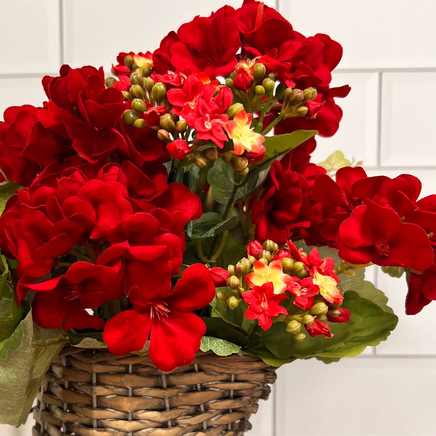 red geraniums in a woven vase with a subway tile background.