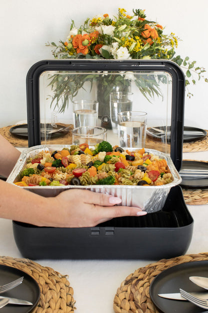 hand putting a foil pan filled with pasta into a grey fancy panz.