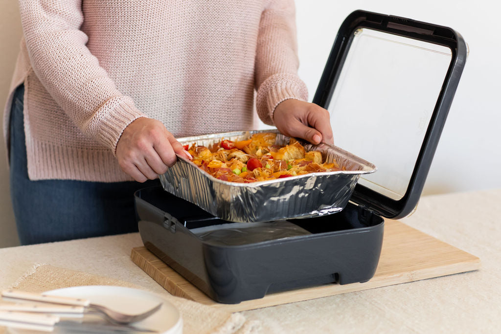 person putting a foil pan filled with a casserole in to a grey fancy panz.