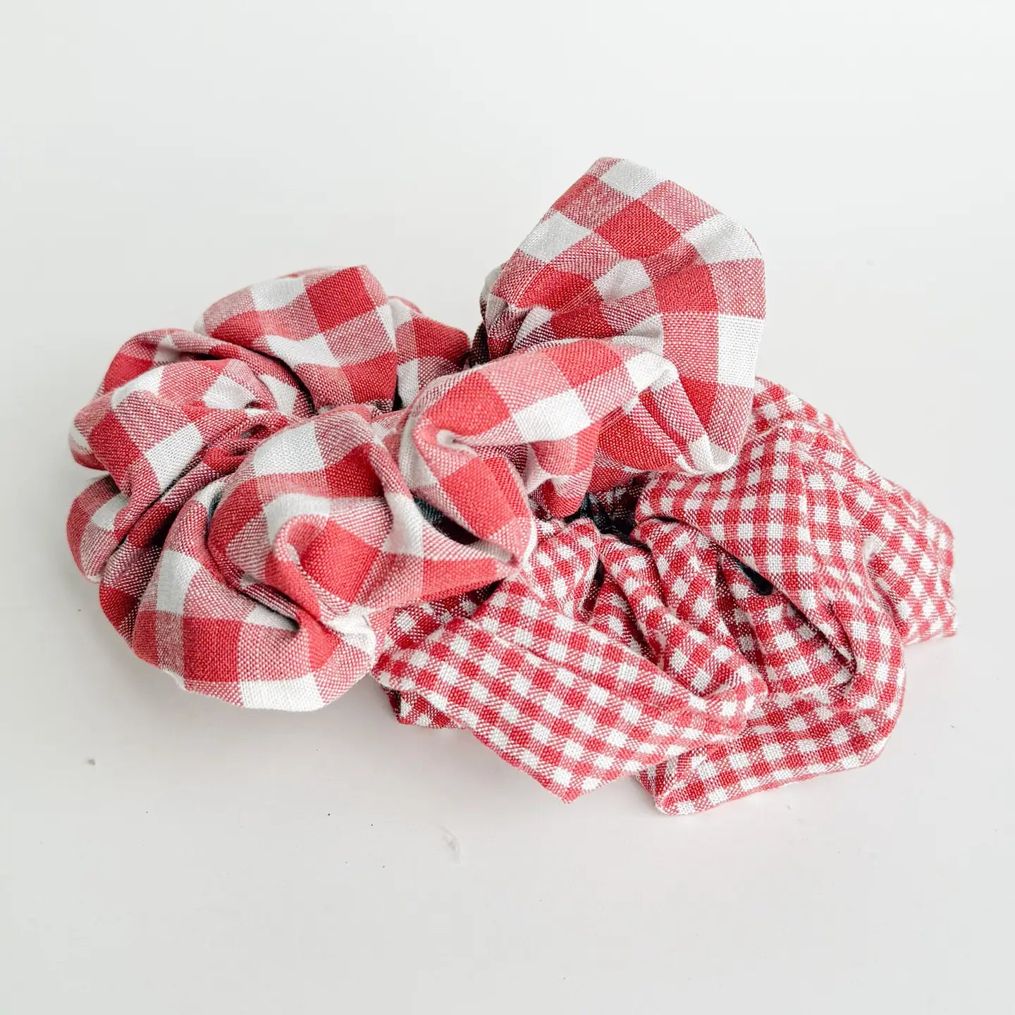 2 red gingham scrunchies, one with large the other small check patterns arranged on a white background