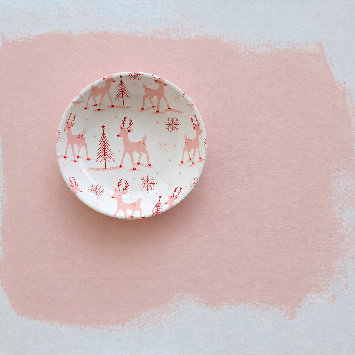 small white bowl with pink reindeer, tree, and snowflake design in the interior shown on a light pink background