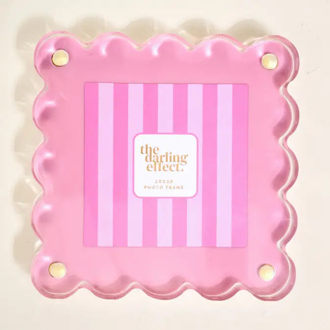 Pink scalloped photo frame with 'the darling effect' branding inside on a beige background