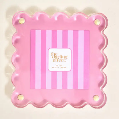 Pink scalloped photo frame with 'the darling effect' branding inside on a beige background