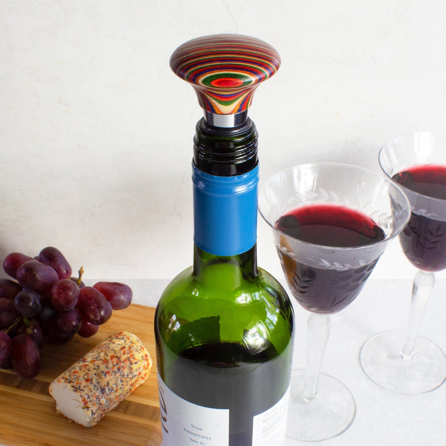 convex marrakesh bottle stopper on a bottle of wine set on a table with glasses of wine and grapes.
