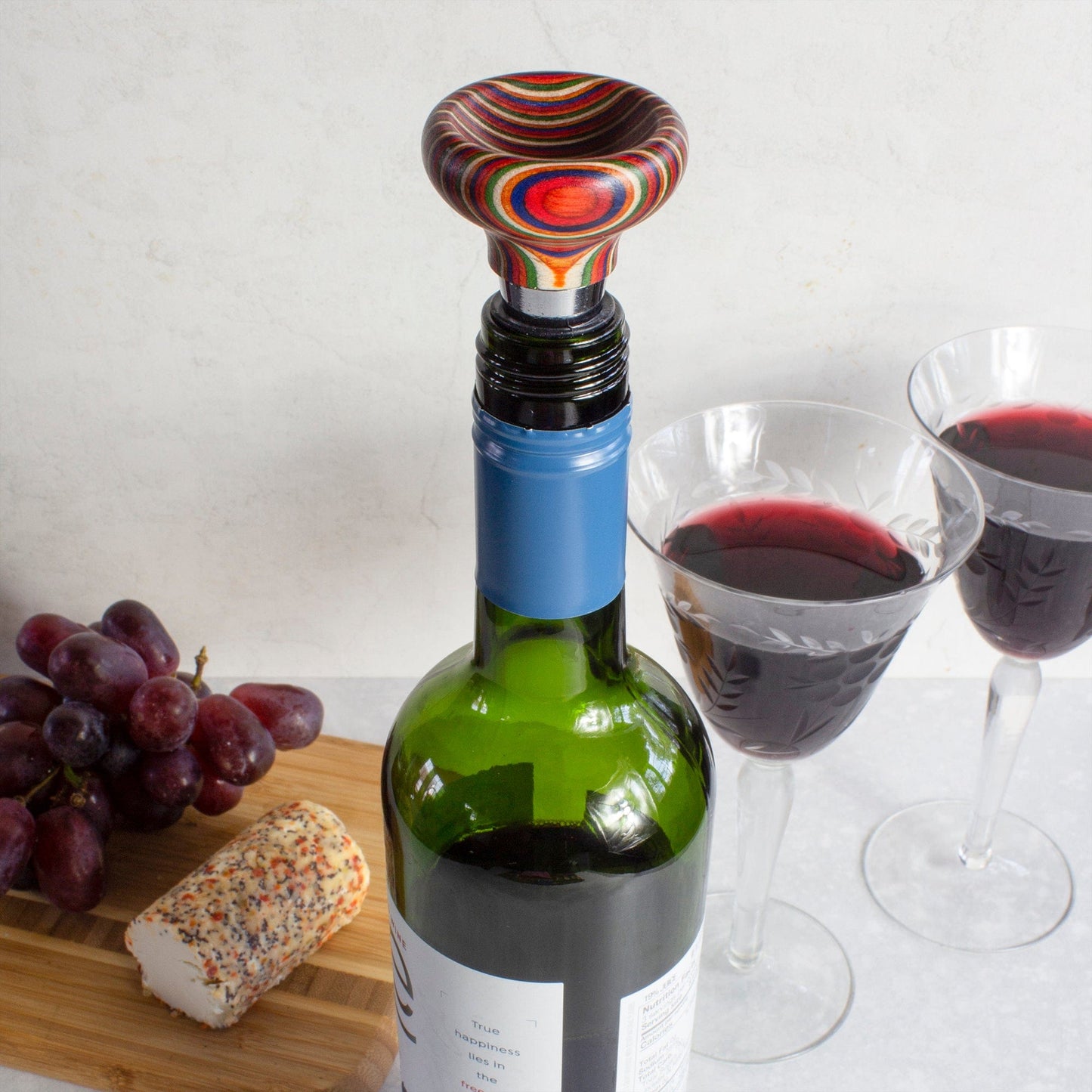 concave marrakesh bottle stopper on a bottle of wine set on a table with glasses of wine and grapes.