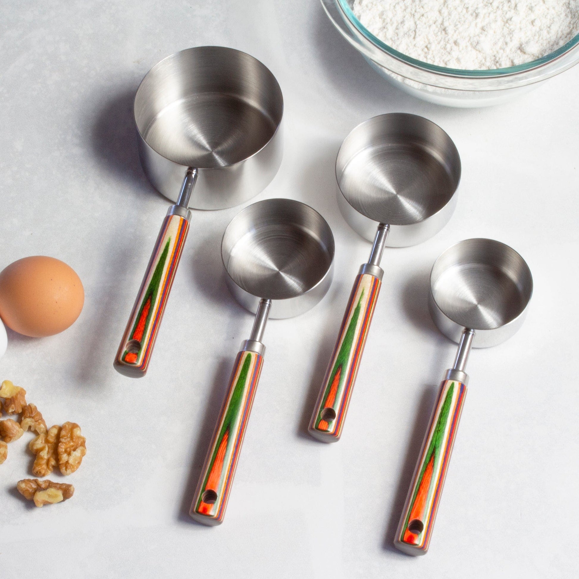 4 sizes of marrakesh measuring cups arranged on a countertop with flour, eggs, and nuts.