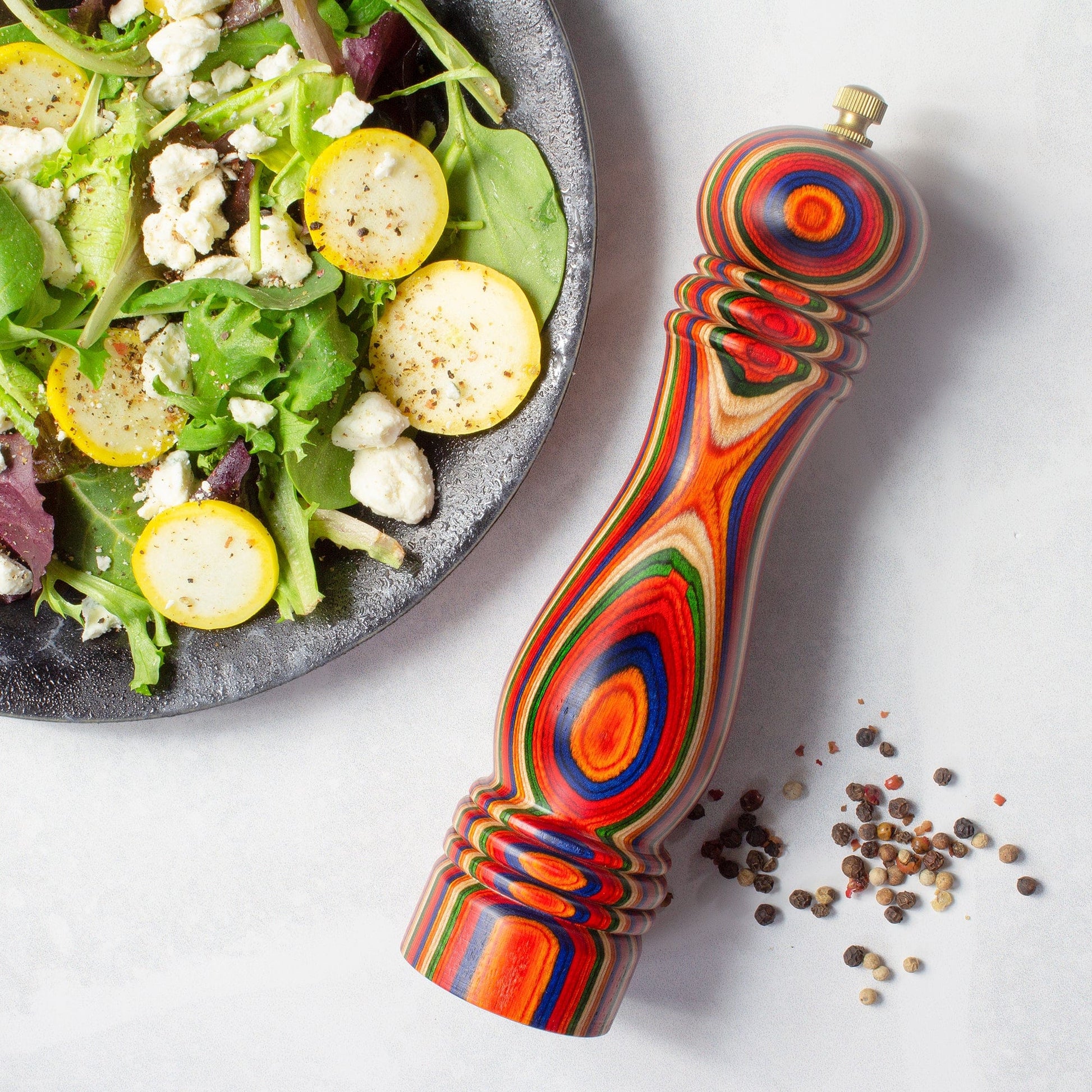 marrakesh pepper grinder layign on a table next to a bowl of salad.