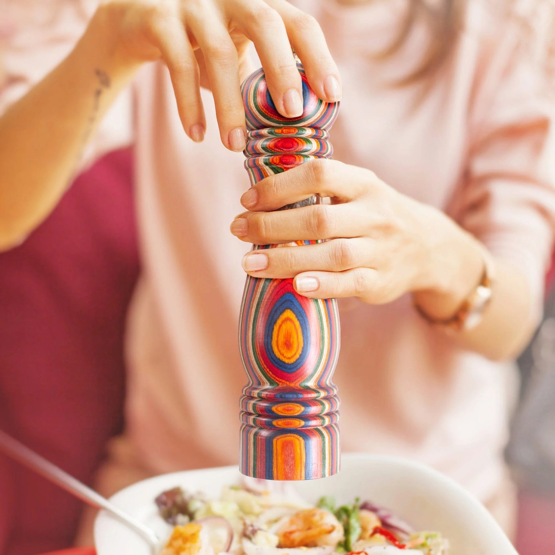 hands using marrakesh pepper grinder to grind pepper over a plate of food.