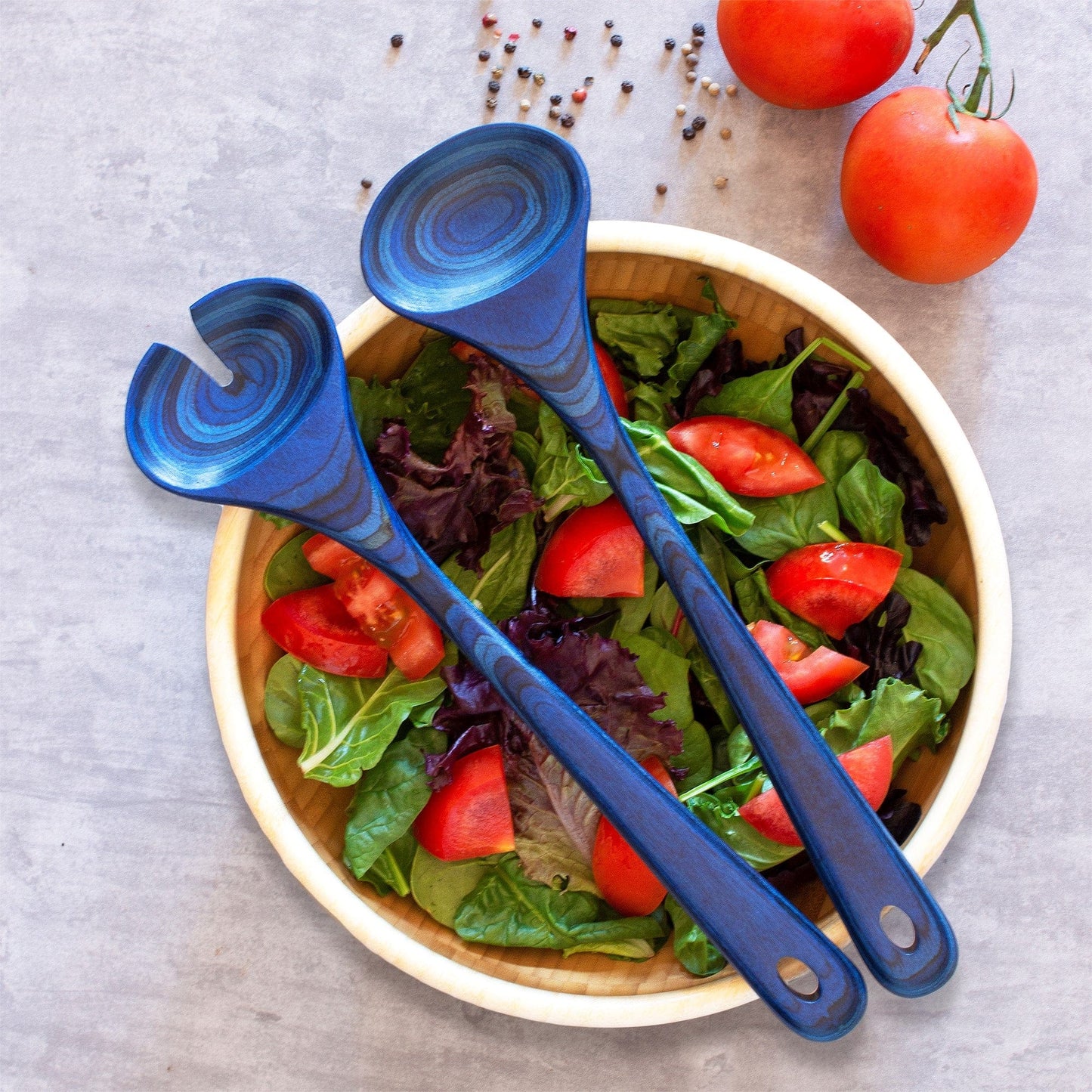 malta serving set laying across a large bowl filled with salad.