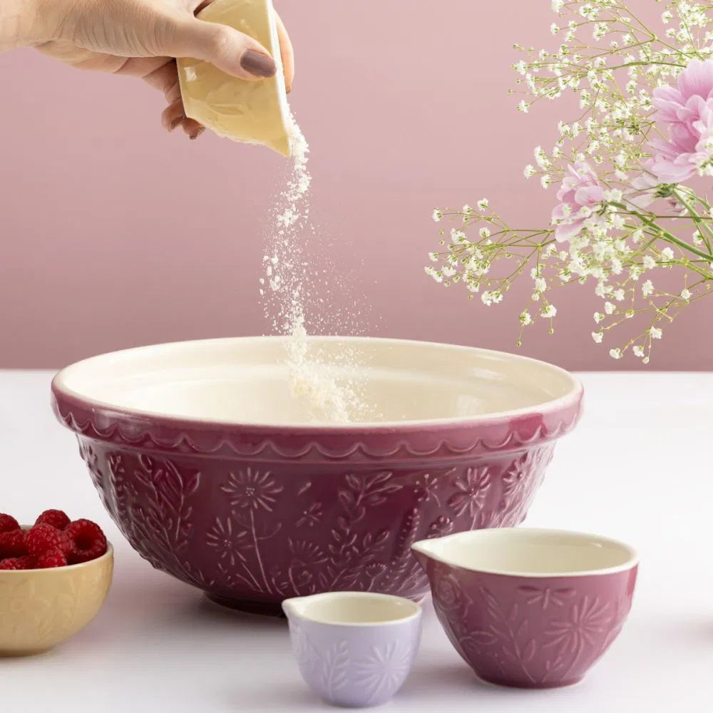 2 measuring cups set on a counter with a mixing bowl and a hand pouring ingredients from another measuring cup into the bowl.