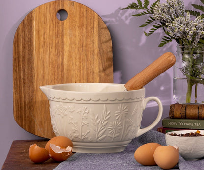 In the Meadow Cream Floral Batter Bowl set on a wooden counter arranged with a cutting board, eggs, and a vase filled with flowers.
