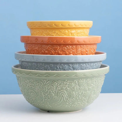 Stack of four ceramic mixing bowls in green, blue, orange, and yellow on a white surface with a blue background.
