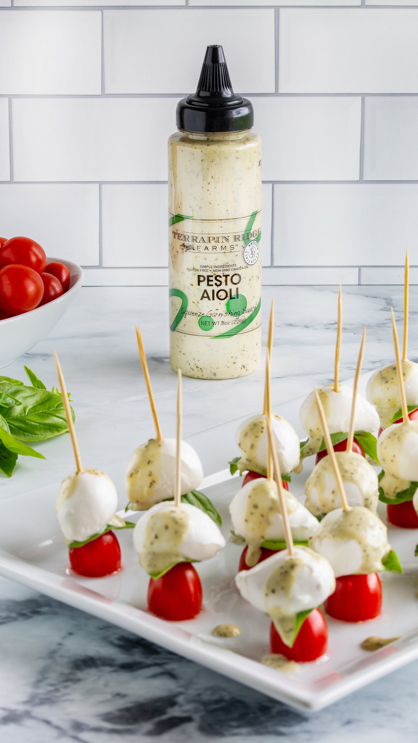 bottle of Pesto Aioli on a counter with a tray of tomato and cheese appetizers.