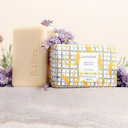wrapped bar of Lavender Goat Milk Bar Soap and an unwrapped bar of soap arranged with lavender flwoers.