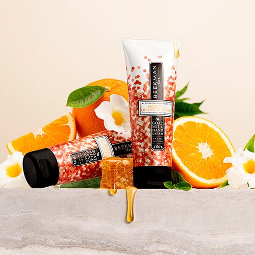 tubes of Honey & Orange Blossom Hand Cream arranged with a honey comb, orange wedges, and blossoms.
