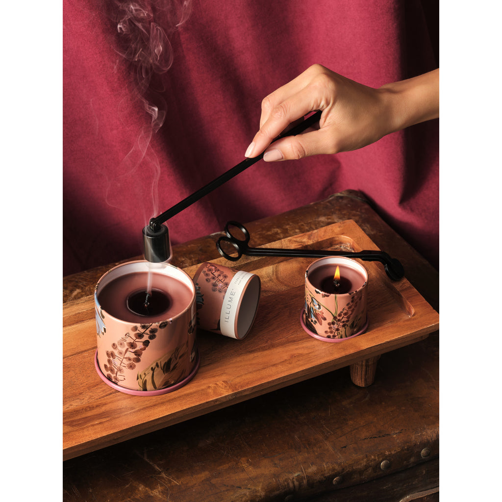 illustration of a womans hand holding the black candle snuffer and putting out candles that are resting on a rectangle wooden tray